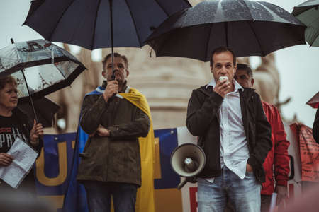 Lisbon, Portugal - March 20, 2022: a protest action in support of Ukraine, against Russian invasion and aggressive war: a stage with protesters with umbrellas under the heavy rain, man with megaphoneのeditorial素材