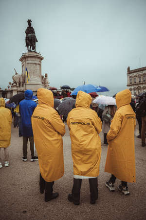Lisbon, Portugal - March 20, 2022: protest action in support of Ukraine, against Russian invasion and war: three protesters in yellow raincoats on the square in front of the stage and the monumentのeditorial素材