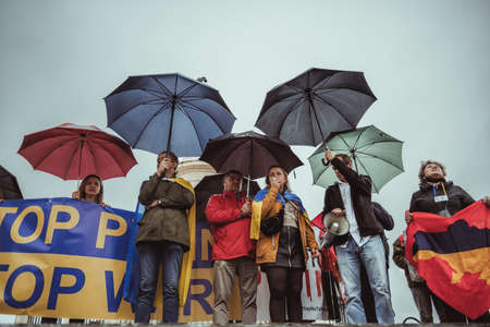 Lisbon, Portugal - March 20, 2022: protest action in support of Ukraine, against Russian invasion and war: a stage with protesters with umbrellas under the rain: woman speaking using a loud-hailerのeditorial素材
