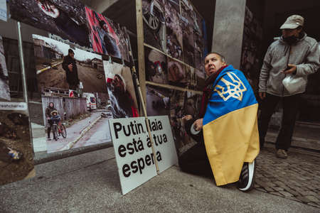Lisbon, Portugal - April 6, 2022: a protest action following the war crimes in Bucha: man wrapped in a Ukrainian flag is installing a street photo exhibition with images after the Russian invasionのeditorial素材