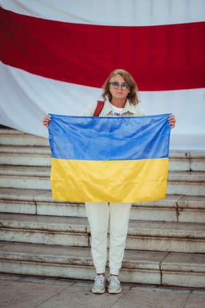 Lisbon, Portugal - March 19, 2022: a Belorussian manifestation in support of Ukraine, against invasion and aggressive war: a woman holding Ukrainian flag while standing against the Byelorussian flagのeditorial素材