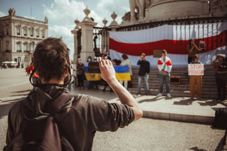 Lisbon, Portugal - March 19, 2022: a Belorussian manifestation in support of Ukraine, against invasion and aggressive war: selective focus man with a smartphone and cigarette filming the protestersのeditorial素材