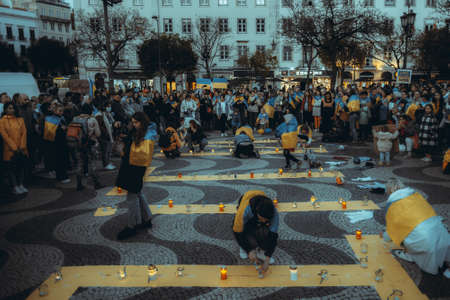 Lisbon, Portugal - April 20, 2022: protest rally dedicated to saving the Ukrainian city of Mariupol from the Russian aggression; women wrapped in flags are lighting candles in memory of the deadのeditorial素材