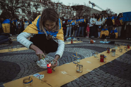 Lisbon, Portugal - April 20, 2022: protest rally dedicated to saving the Ukrainian city of Mariupol from the Russian invasion; a woman wrapped in Ukrainian flag lighting candles in memory of the deadのeditorial素材
