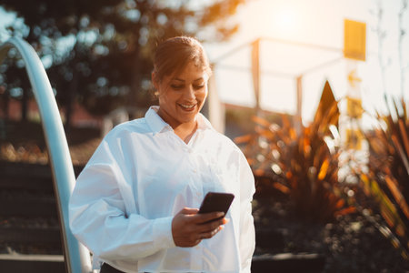 Portrait of a dazzling smiling plus-size Hispanic woman using her cellphone in a park on a sunny day; an adult cheerful Caucasian female with a smartphone outdoors, a copy space place on the rightの写真素材