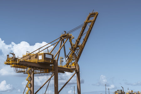 Close-up view of a heavy huge harbor crane in front of a beautiful skyscape, with a big cabin, many stairways, cables, and passages with fences on its top; a copy space area on the rightの写真素材