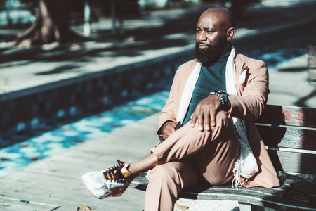 A portrait of a handsome bald bearded black senior man in a fancy pinkish tailored suit sitting on a...