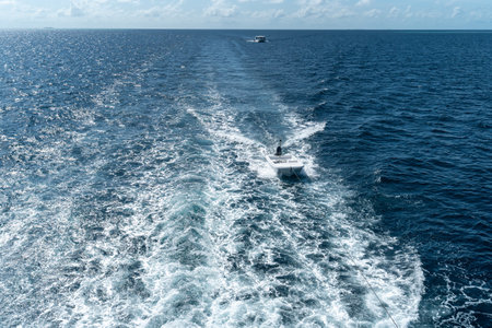 View from the boat stern of the wake (wash) effect on the water from the motor placed on the transom of a luxurious safari vessel sailing between Maldives islands with a tied tiny dinghy behind itの写真素材