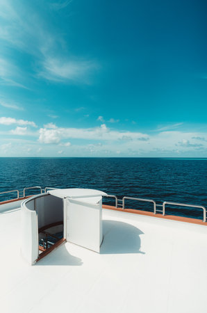 A vertical wide-angle shot of a bright diving safari yacht top deck with a selective focus on the ladder leading downstairs to the middle deck; the ocean and a blue sky in the backgroundの写真素材