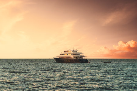 View of a luxury yacht floating on the waves with a stunning evening skyscape in the background; a multideck safari boat in the ocean on a sunset with a dramatic sky of a golden hourの写真素材