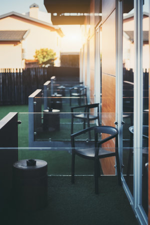 A vertical shot with a shallow depth of field and a selective focus on the chair and an ashtray placed on the modern balcony of a hotel with a row of identical balconies in the defocused backgroundの写真素材
