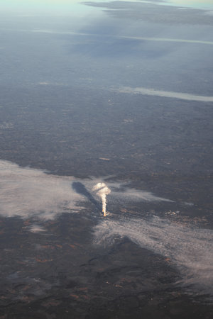 The photograph taken from the window of an airplane depicts a thermal power plant emitting greenhouse gases. A grey, cloudy day in the French countryside with a cogeneration plant from high aboveの写真素材