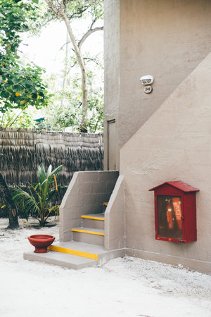 Tropical design house entrance with sand on the floor, reed fencing the residence, plants, a firefighting tool, a bowl for foot washing, yellow lines highlighting the steps of the stairsの写真素材