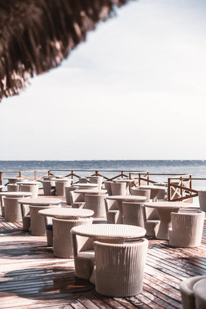 View of an empty outdoor restaurant area filled with wicker tables and chairs, bellow it a wet...