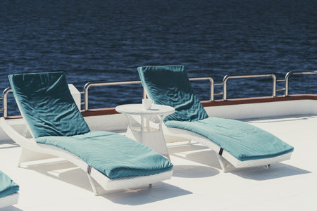 A wide-angle shot of two lounge chairs with blue cushions on top of them and a small white color...