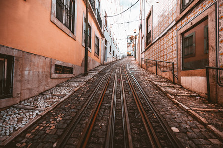 A wide-angle view of a road with a retro two-lane tramway over paving stone on a narrow street in a picturesque old neighborhood in shades of salmon on the walls and tiles in Lisbon, Portugalの写真素材