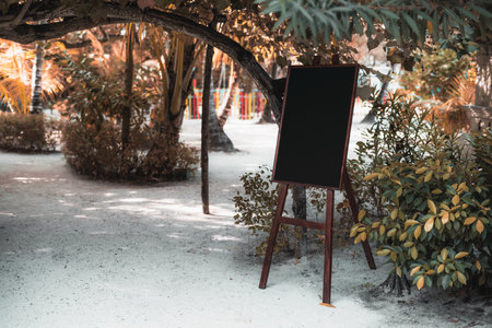A blank chalkboard sign stands on a picturesque sandy beach with palm trees, ready to showcase messages or promotions; Mockup for creative advertising, wedding announcements, inspirational quotes, etcの写真素材