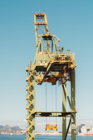 Vertical zoomed-in view of a heavy yellow industrial crane machinery with the blue cloudless sky in the background, with a big cabin, many stairs, cables, and passages with fences on its topの写真素材