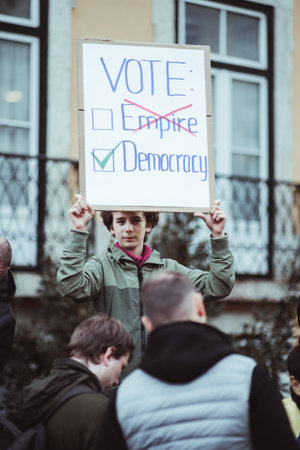 Lisbon, Portugal - February 24, 2023: Amidst a crowd at the one-year anniversary of the war in Ukraine, a young boy stands, holding a placard with a powerful message advocating for democracy; verticalのeditorial素材