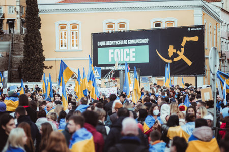 Lisbon, Portugal - February 24, 2023: Selective focus captures a passionate crowd of anti-war protesters, proudly holding up Ukrainian flags to mark the one-year anniversary of the armed conflictのeditorial素材