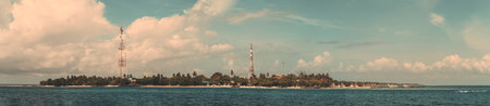 A breathtaking panoramic view of the coastline of a magnificent island in the Maldives, featuring lush vegetation and two signal repeater towers that stand out against the natural landscapeの写真素材