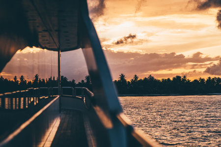 An orange sunset in the Maldives glows, creating a breathtaking vista from the deck of a safari yacht; trees in the background frame the scene, while the sea captures the last rays of lightの写真素材