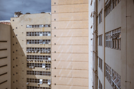A snapshot of the inner corner of two housing apartments painted in a soft peach hue reveals several tiny square windows, and multiple air conditioning unit compressors on a cloudy day; wide angleの写真素材