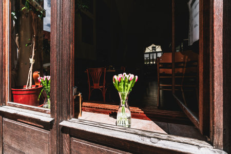 On a wooden window sill, a glass jar brims with crystal-clear water, cradling a bouquet of pink tulips. As the warm Prague sunlight filters through the window, the flowers bask in their gentle glowの写真素材