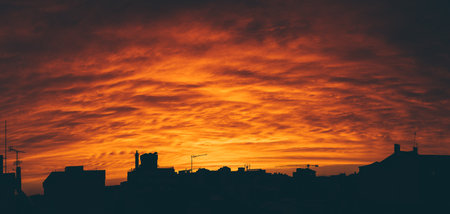 Panoramic view of a bright orange sunset, contrasting the silhouettes of the city's buildings and houses; the dusty scenario envelops the town in an almost otherworldly hazeの写真素材