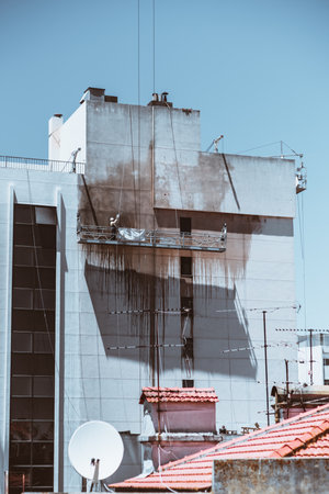 A vertical shot captures an apartment wall being cleaned; Blackened water drips down the building, creating a striking contrast against the white paint, the sky is clear blueの写真素材