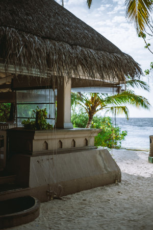 Sunny day at a sandy beach bar built on sandstone with a thatched roof. Coconut palm trees with green leaves can be seen in the background, viewing the sea, providing a natural touch to the sceneの写真素材