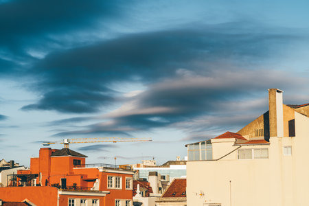 A blue sky with spotted dark clouds, and a big bright orange house stands out from the other in the scene, creating a vibrant contrast. The bright colors add a touch of playfulness to the city's viewの写真素材
