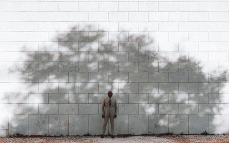 Lisbon; a black man standing elegantly and serenely in front of a white tile wall texture background, wearing a cream suit. A shadow of a big tree is showing on him and the wall behind himの写真素材