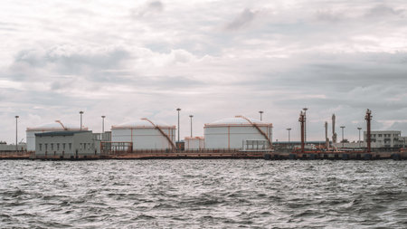Gray sea waters stretch in the foreground, with aviation fuel storage tanks at Male's airport in the background, showing the vital infrastructure of the Maldivesの写真素材