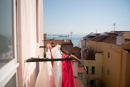 View from a Lisbon apartment balcony, showing colorful clothes hanging to dry with a backdrop of...