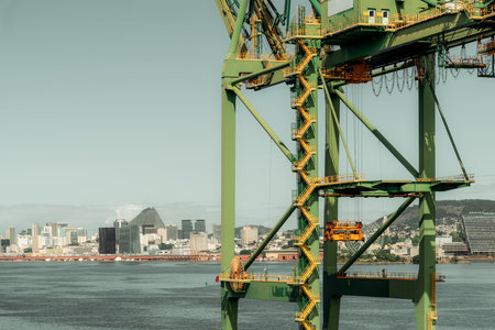 Green industrial crane structure with yellow accents at the port, set against the backdrop of Rio de Janeiro city skyline with iconic Sugarloaf Mountain and water in the foregroundの写真素材