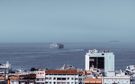 Aerial view of a container ship sailing in the ocean with residential buildings and rooftops in the...