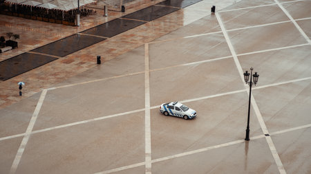 Aerial view of a large, mostly empty public square on a rainy day, featuring a lone person with an umbrella and a police car. The wet pavement of Lisbon Commerce Square reflects surrounding buildingsの写真素材