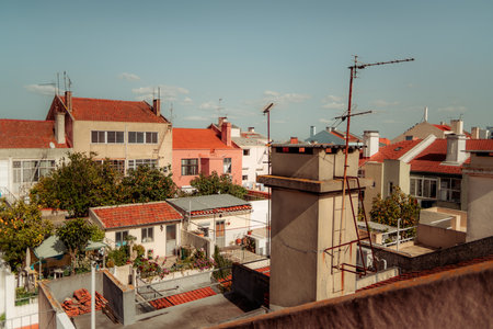 Lisbon cityscape featuring traditional residential buildings with red tiled roofs, visible antennas, and lush gardens. A clear blue sky and sunlight highlight the urban neighborhood.の写真素材