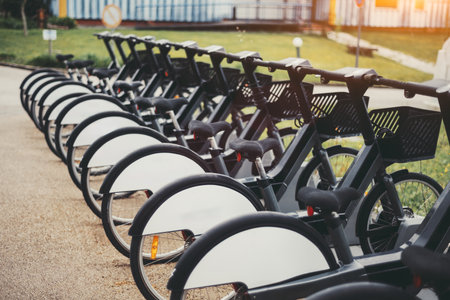 Row of modern electric black bicycles parked in an urban bike-sharing station, featuring basket-equipped handlebars, comfortable saddles, and sleek white fenders ready for public use in a city settingの写真素材