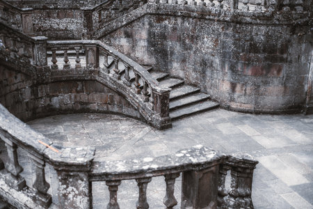 Ancient stone staircase with weathered balustrades in a circular architectural design. Moss and...
