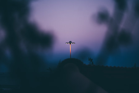 Telephoto shot of a street lamp stands illuminated against a dusk sky, creating a serene and atmospheric scene. Soft shadows frame the image, with a smooth gradient of blue to purple in the backgroundの写真素材