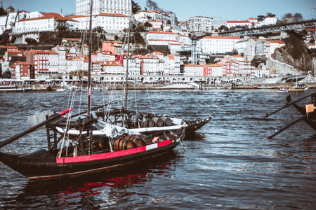 Traditional Portuguese Rabelo boat loaded with wooden wine barrels, docked on the Douro River in Porto, Portugal, with colorful Ribeira waterfront buildings in the backgroundの写真素材