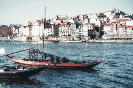 Traditional wooden boats with wine barrels floating on the Douro River, Porto, Portugal, with colorful historic Ribeira district houses in the background under a clear skyの写真素材