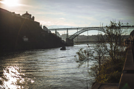 The Dom Luis I Bridge in Porto, Portugal, spanning the Douro River, with sunlit water, silhouetted...