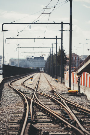 Vertical telephoto shot of railway tracks with multiple switches and overhead electric lines in an urban setting. Perspective view with converging rails, industrial background, and metal polesの写真素材