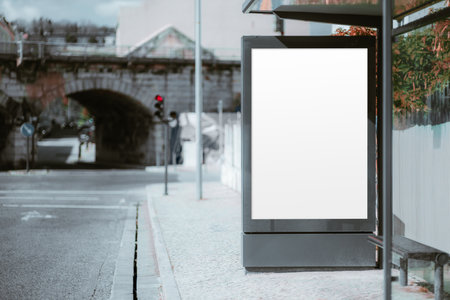 Blank bus stop advertising mockup in urban setting. Empty vertical billboard with white screen for branding or commercial ad placement. Blurred city street backgroundの写真素材