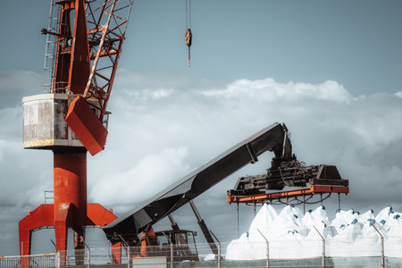 Large industrial crane with a conveyor system lifting heavy white bulk bags at a port. The rusted metal structure contrasts with the cloudy sky, emphasizing logistics and cargo transportの写真素材
