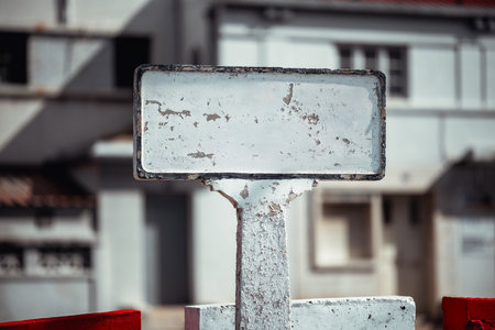 Weathered blank concrete sign with peeling white paint on a rough-textured post, set against an urban background with industrial buildings. Ideal for mockups, text overlays, and design projectsの写真素材