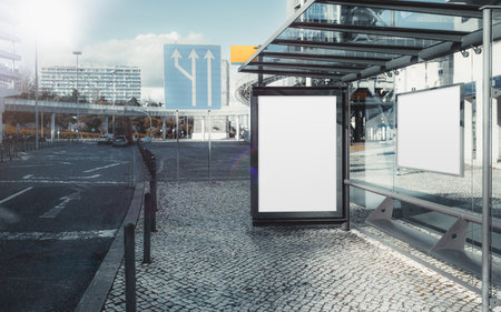 Bus stop with two blank advertising billboards for mockup purposes. Urban setting with glass shelter, paved sidewalk, traffic signs, and modern buildings in the backgroundの写真素材